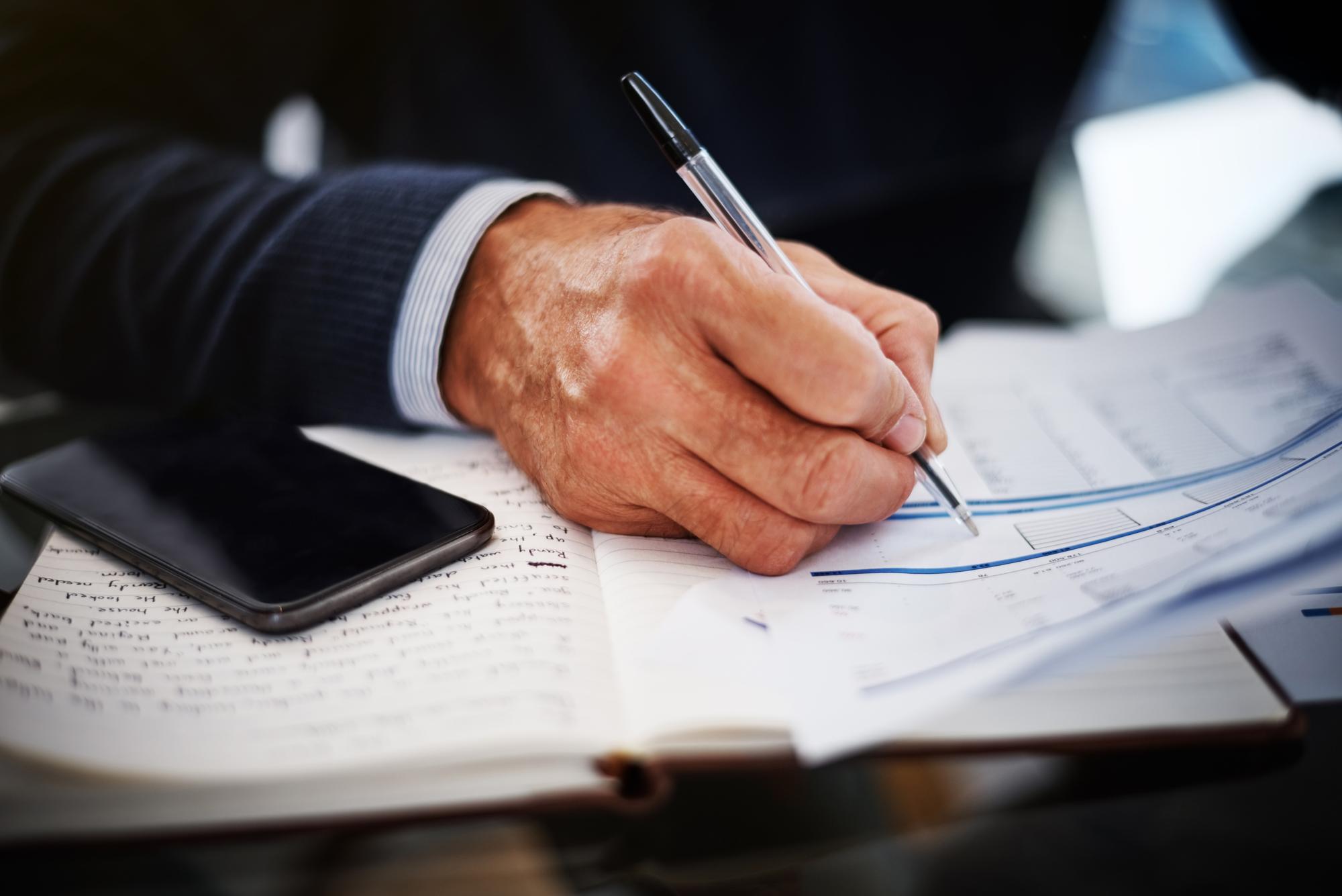 Detail: Hand mit Stift über Verträgen